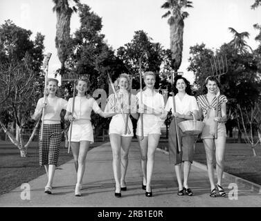 États-Unis : c. 1960 six femmes marchant sur un sentier transportant des outils de jardinage. Banque D'Images