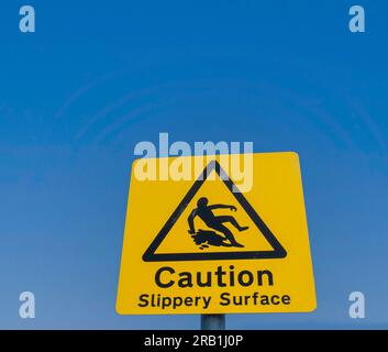 Signalisation pour une surface glissante, un panneau jaune posé contre un ciel bleu clair. Banque D'Images