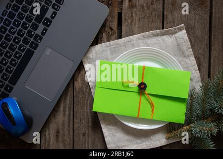 enveloppe cadeau verte se trouve sur la table près de l'ordinateur portable et une branche de pin, un cadeau pour la nouvelle année Banque D'Images