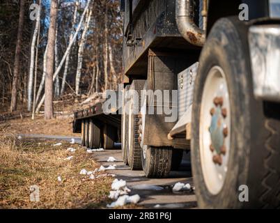 Pneus et roues et le côté droit d'un camion et d'une remorque garés sur une route pavée par un après-midi ensoleillé, avec des morceaux de neige fondants sur le sol au travail Banque D'Images