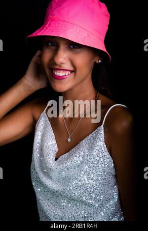 Belle jeune fille posant pour la photo en studio. Port d'un chapeau rose. Isolé sur fond noir. Banque D'Images