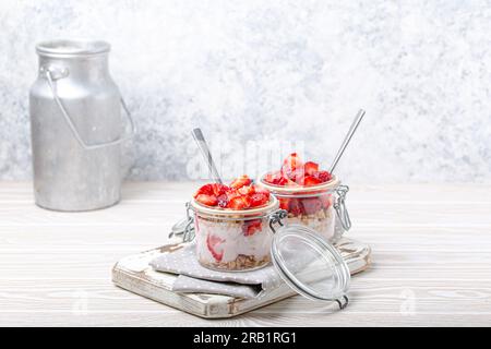 Parfait avec fraises, yaourt et granola en verre transparent, jarres Mason sur fond de bois rustique blanc, vue d'angle et boîte de lait en aluminium Banque D'Images