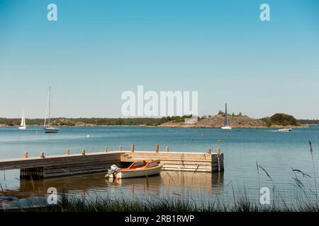 Archipel de Stockholm au coucher du soleil avec un petit bateau amarré à la jetée avec des voiliers ancrés en arrière-plan Banque D'Images