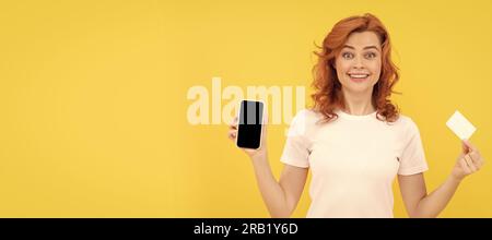 une jeune femme excitée a isolé un fond surjaune en utilisant un téléphone portable tenant une carte de crédit. Femme isolée visage portrait, bannière avec espace de copie de maquette Banque D'Images