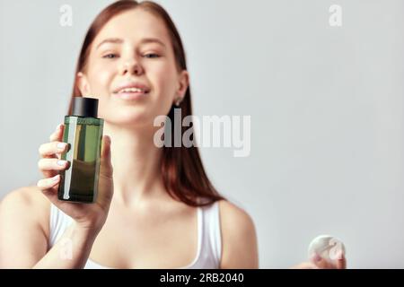 Jeune fille souriante attrayante avec de longs cheveux bruns utilise une lotion pour le visage. Femme caucasienne prenant soin de la peau pour maintenir son appe jeune et sain Banque D'Images