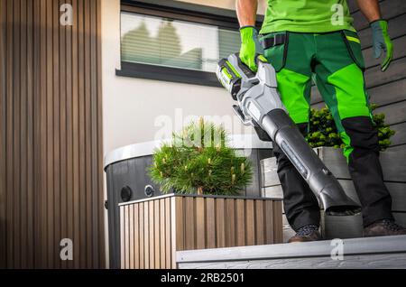 Gros plan de jardinier professionnel nettoyage du jardin d'arrière-cour à l'aide de souffleur d'air électrique tenu à la main. Thème de l'équipement motorisé industriel. Banque D'Images