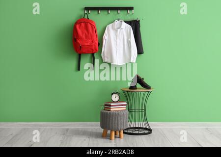 Rack avec uniforme scolaire élégant, banc et table près du mur vert dans la chambre Banque D'Images