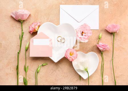 Composition avec enveloppes, carte vierge, anneaux de mariage et fleurs d'eustoma sur fond beige Banque D'Images