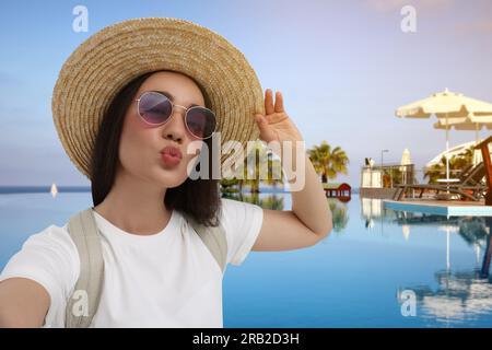 Jeune femme souriante aux lunettes de soleil et chapeau de paille prenant selfie à la station Banque D'Images