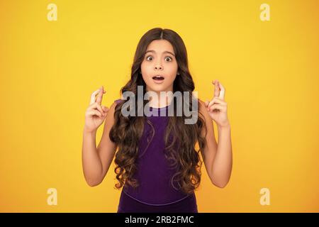 Adolescente en colère, contrariée et malheureuse émotion négative. Bonne adolescente croise les doigts, anticipe entendre de bonnes nouvelles, isolé fond jaune Banque D'Images