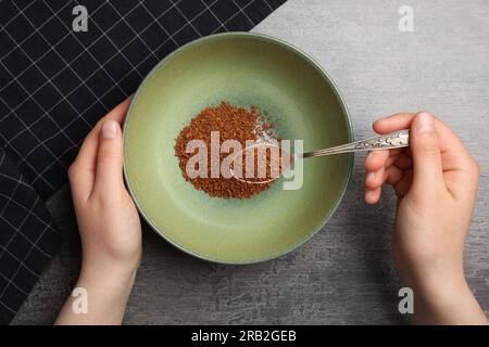 Femme versant des granules de café instantané dans le bol à la table grise, vue de dessus Banque D'Images