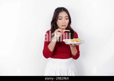 Jeune femme dégoûtée en pull décontracté tient la pomme de terre frites de restauration rapide avec geste dégoûté isolé sur fond blanc. Mode de vie des gens Banque D'Images