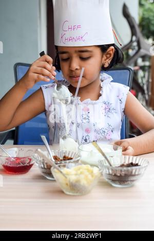 Mignonne fille de chef indien préparant le plat de sundae dans le cadre de la cuisson sans feu qui comprend la crème glacée à la vanille, brownie, poudre de coco, frui fraîchement haché Banque D'Images