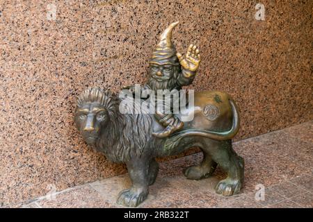 Nain chevauchant un chapeau de lion de couchage assis sur un lion et saluant. Petites figures en bronze de gnomes dans les rues de Wroclaw. Europe figurine miniature en bronze d'un gnome. Symbole de Wroclaw. Attraction touristique Banque D'Images