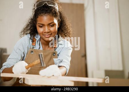 Smart Happy Woman marteau de travail en bois sur le projet de planche en bois meubles à la maison diy dans l'atelier. Banque D'Images