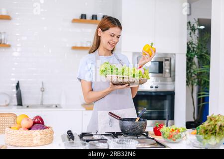 Heureuse jeune femme faisant la salade. Les gens mangent des aliments sains. Vegan Lady dans Kitchen Home. Mangez des légumes pour suivre un régime. Préparez un repas diététique à Island Stove. Banque D'Images