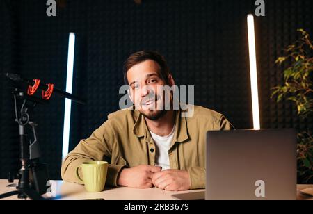 Hôte radio souriant dans le microphone de studio à la station de radio avec des lumières au néon regardant la caméra Banque D'Images