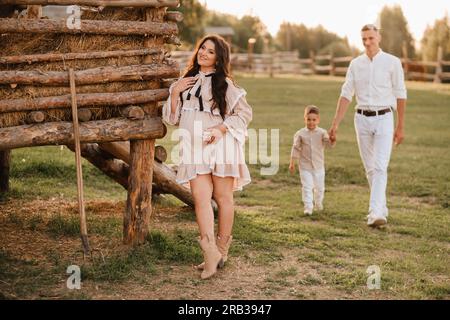 Une famille élégante dans la campagne au coucher du soleil. Une femme enceinte avec son mari et son fils dans la nature. Banque D'Images