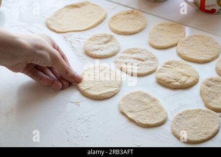 les mains des femmes pétrient la pâte crue sur une table blanche dans la cuisine, pâte Banque D'Images