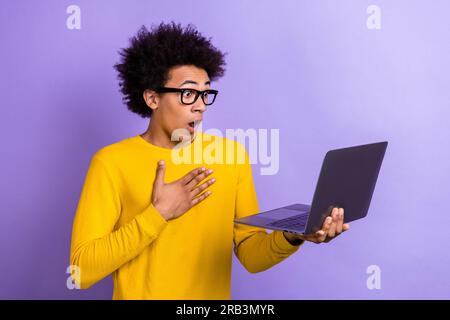 Photo du jeune homme surpris mains poitrine choqué mauvaises nouvelles lisant l'information ordinateur portable sur l'inflation isolé sur fond de couleur violette Banque D'Images