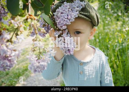 Portrait de printemps de mignon garçon en bas âge avec la branche de lilas en fleurs. Banque D'Images