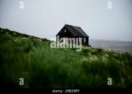 Petite église noire située sur une pente herbeuse Banque D'Images