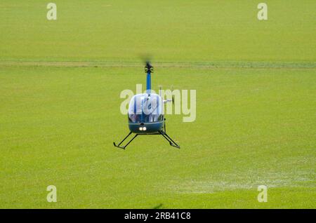 Hélicoptère Robinson R-22 planant bas à un événement ailes et roues dans la campagne à Heveningham Hall. Piste d'atterrissage en herbe rurale dans le Suffolk Banque D'Images