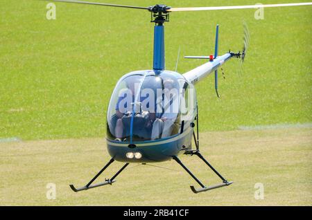 Hélicoptère Robinson R-22 planant bas à un événement ailes et roues dans la campagne à Heveningham Hall. Piste d'atterrissage en herbe rurale dans le Suffolk Banque D'Images