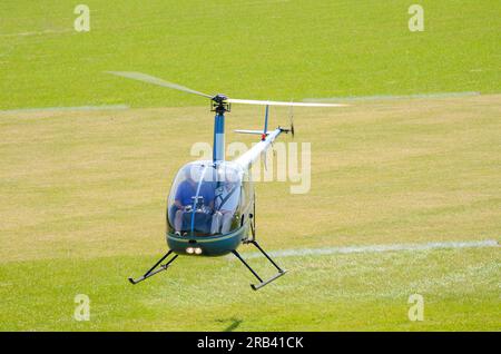 Hélicoptère Robinson R-22 planant bas à un événement ailes et roues dans la campagne à Heveningham Hall. Piste d'atterrissage en herbe rurale dans le Suffolk Banque D'Images