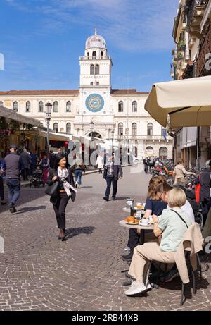 Les gens dans un café de rue, vue sur la rue sur la place Piazza dei Signori, avec son horloge médiévale sur une journée ensoleillée de printemps, Padoue Veneto Italie Europe. Voyages Banque D'Images