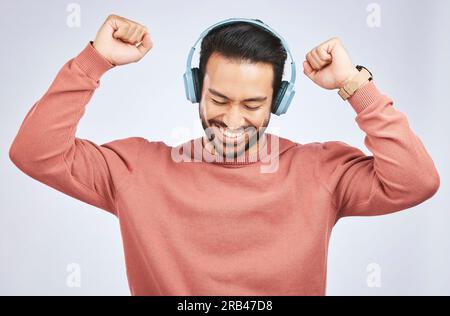 Homme, écouteurs et danse à la musique en studio, fond blanc et célébrer avec énergie. Heureux, excité et jeune modèle masculin asiatique écoutant de l'audio Banque D'Images