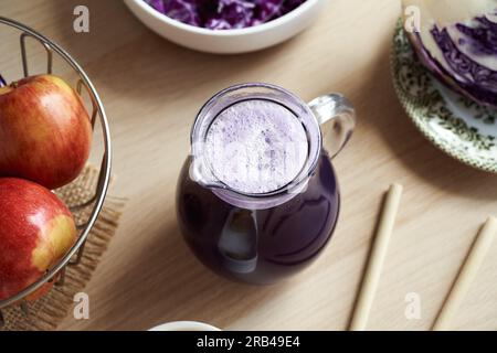 Jus de chou violet dans une cruche en verre avec des pommes et des pailles de bambou Banque D'Images