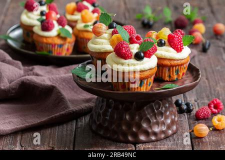 Cupcakes à la crème au beurre et au caillé de framboise, décorés de baies sur une surface en bois. Banque D'Images