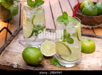 Cocktail Mojito avec des tranches de citron vert et des feuilles de menthe à l'extérieur sur plateau en bois Banque D'Images