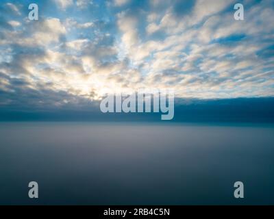 Une photo aérienne saisissante capture le spectacle époustouflant du soleil se levant au-dessus d'une couverture de nuages en peluche. L'image éthérée évoque un sentiment écrasant de paix, d'immensité et la grandeur des miracles quotidiens de la nature. Vue aérienne : lever de soleil majestueux au-dessus des nuages. Photo de haute qualité Banque D'Images