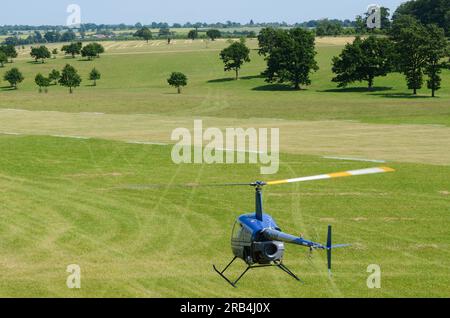 Robinson R-22 planant bas au-dessus d'une piste d'atterrissage en herbe lors d'un événement Wings and Wheels dans la campagne à Heveningham Hall. Campagne dans le Suffolk. Parc Banque D'Images