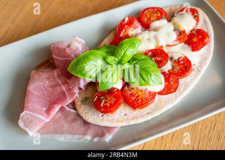 Bruschetta avec tomates cerises fraîches, fromage mozzarella et jambon fumé avec feuilles de basilic garnir sur pain pita Banque D'Images