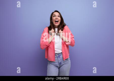 une femme brunette heureuse, dans un style informel, se réjouit sur fond de studio Banque D'Images