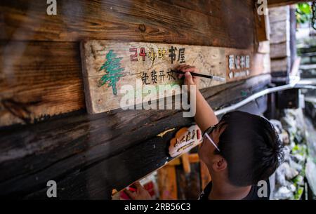 (230707) -- GONGSHAN, 7 juillet 2023 (Xinhua) -- Gan Wenyong insiste sur un slogan indiquant « bibliothèque gratuite 24 heures » à la bibliothèque « Banshan Huayu » dans le village de Qiunatong de la municipalité de Bingzhongluo dans le comté autonome de Gongshan Dulong et nu, préfecture autonome Lisu de Nujiang, province du Yunnan, au sud-ouest de la Chine, le 6 juillet 2023. La rivière Nujiang, descendant des montagnes Tanggula sur le plateau Qinghai-Tibet, se fraie un chemin à travers les majestueuses montagnes du Yunnan où se forme un magnifique canyon. Niché à la pointe nord du canyon de la rivière Nujiang est le village de Qiunatong, ho Banque D'Images