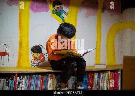 (230707) -- GONGSHAN, 7 juillet 2023 (Xinhua) -- Un enfant lit un livre à la bibliothèque 'Banshan Huayu' dans le village de Qiunatong, dans le canton de Bingzhongluo, dans le comté autonome de Gongshan Dulong et nu, préfecture autonome de Lisu de Nujiang, province du Yunnan, au sud-ouest de la Chine, le 5 juillet 2023. La rivière Nujiang, descendant des montagnes Tanggula sur le plateau Qinghai-Tibet, se fraie un chemin à travers les majestueuses montagnes du Yunnan où se forme un magnifique canyon. Niché à l'extrémité nord du canyon de la rivière Nujiang se trouve le village de Qiunatong, qui abrite une bibliothèque unique appelée 'Banshan Huayu Banque D'Images