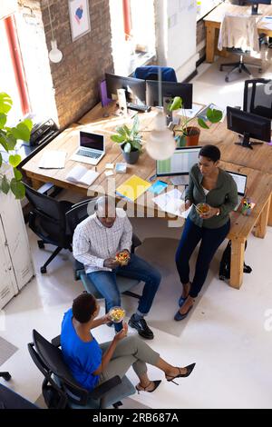 Heureux collègues afro-américains discutant du travail et déjeunant dans un bureau créatif. Affaires, brainstorming, nourriture et travail d'équipe, inchangés. Banque D'Images