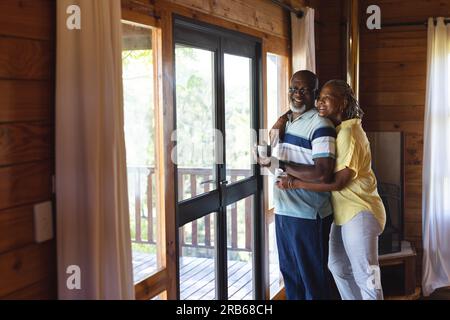 Heureux couple afro-américain senior embrassant et regardant par la fenêtre à la maison. Style de vie senior, détente et retraite, inchangé. Banque D'Images