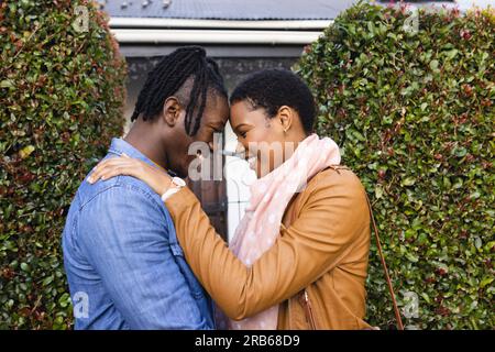Vue latérale d'un couple afro-américain romantique regardant l'un l'autre tout en se tenant à l'extérieur de la maison. Inaltéré, amour, unité, affectueux, heureux, Banque D'Images