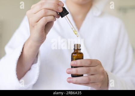 Femme caucasienne portant un peignoir et appliquant de l'huile dans la salle de bain. Vie domestique, soins personnels et mode de vie, inchangés. Banque D'Images