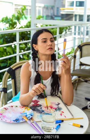 Femme brunette ukrainienne peignant le dessin à l'aquarelle d'une fille asiatique avec un pinceau sur une table avec de l'eau et des peintures Banque D'Images