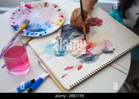 Femme peignant dessin à l'aquarelle de fille asiatique avec pinceau sur une table avec de l'eau et des peintures Banque D'Images