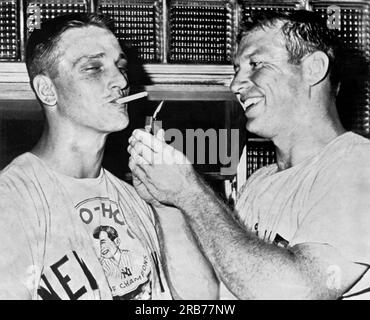 New York, New York : 13 juillet 1961 New York Yankee slugger Roger Maris obtient une lumière pour sa cigarette de son coéquipier Mickey Mantle après qu'ils ont frappé dos à dos dans la première manche contre les White Sox de Chicago. Banque D'Images