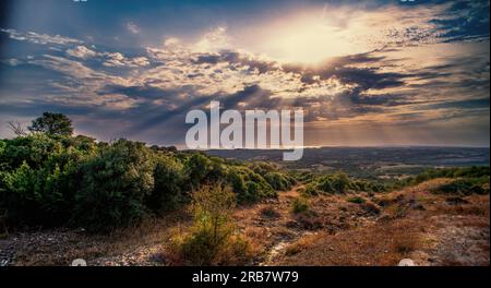 Paysage de collines avec des rayons de soleil sortant des nuages dans une région du nord de la Grèce en été où la mer peut être vue au loin Banque D'Images
