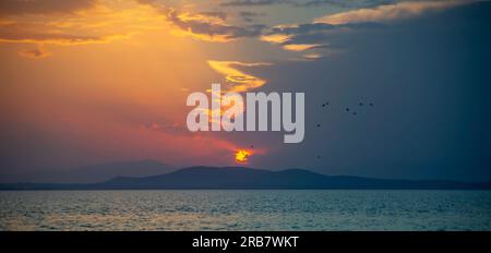 Paysage balnéaire dans une région du nord de la Grèce où le soleil est partiellement caché par les nuages et la moitié du paysage est rouge avec des montagnes dans le di Banque D'Images