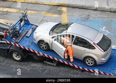 Voiture endommagée chargée sur une dépanneuse par un travailleur. Service de remorquage sur la ville. Concept d'assistance routière Banque D'Images